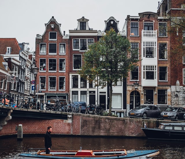 A man in a boat glides through a canal in Amsterdam, with urban buildings standing tall along the banks.