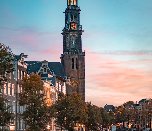 The Westerkerk tower in Amsterdam during sunset, with a soft pink and blue sky.